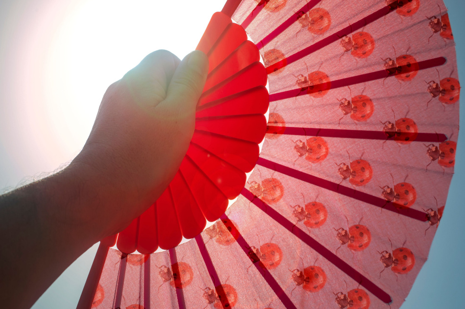 Hand fan covering the sun to cool down and give yourself air in heat alerts. Heat wave heatstroke concept.