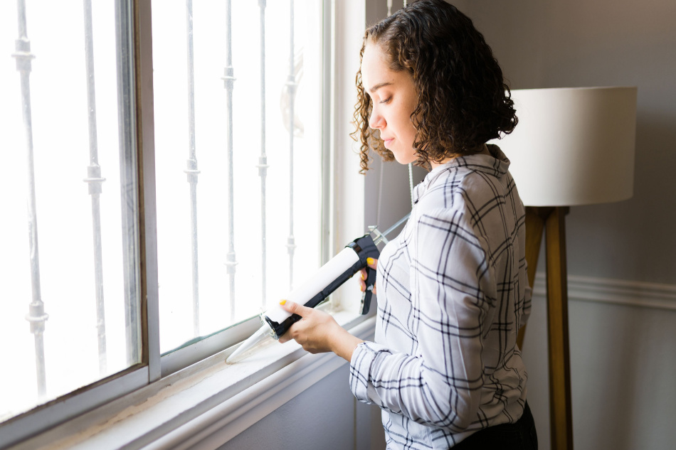 Attractive young woman using silicone sealant on the window and repairing the windows of her house