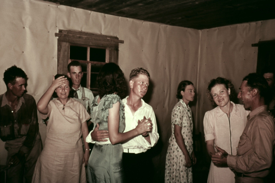 Square dance in rural home in McIntosh County Oklahoma. They dance in a simple interior with butcher paper covered walls
