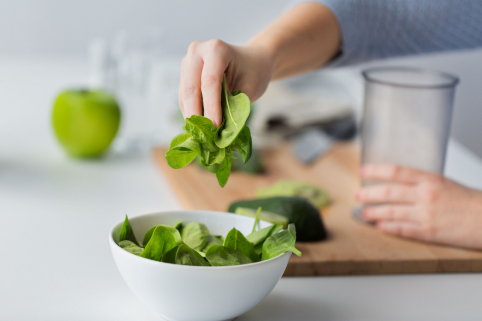 close up of woman hand adding spinach leaves to bowl