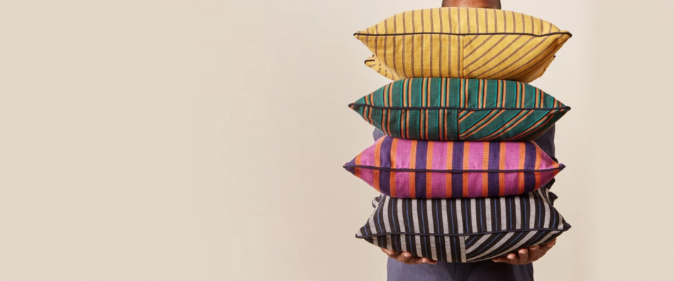 Person holding pile of brightly colored patterned pillows.