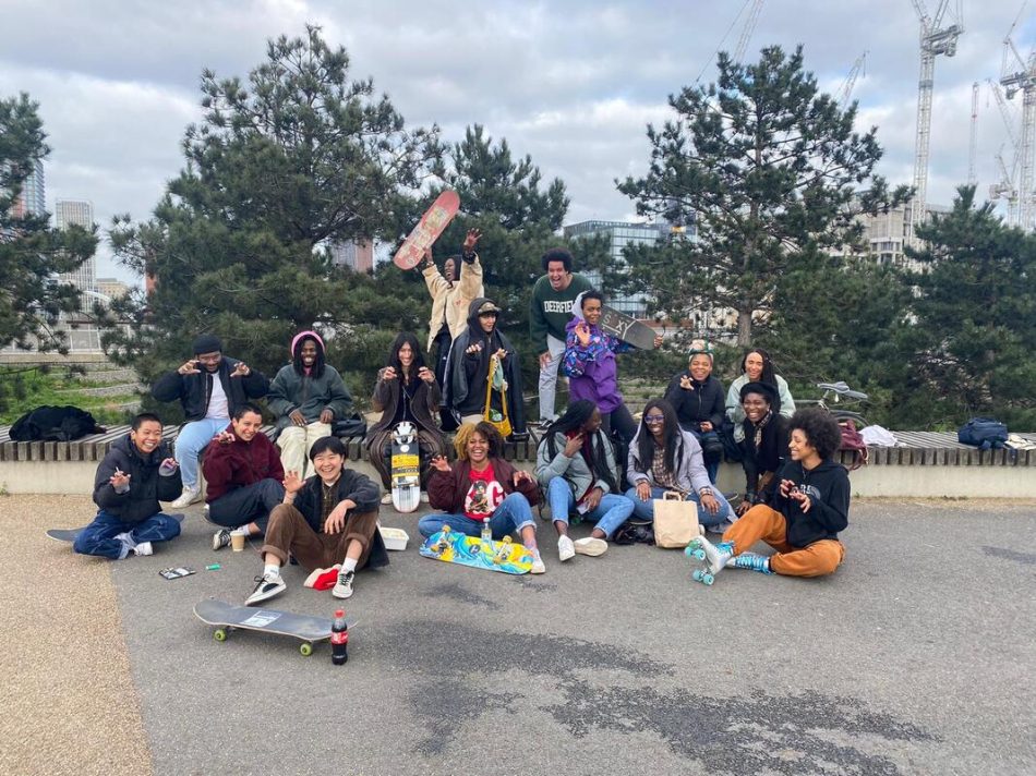 A large group of minority skateboarders pose with their skateboards outside
