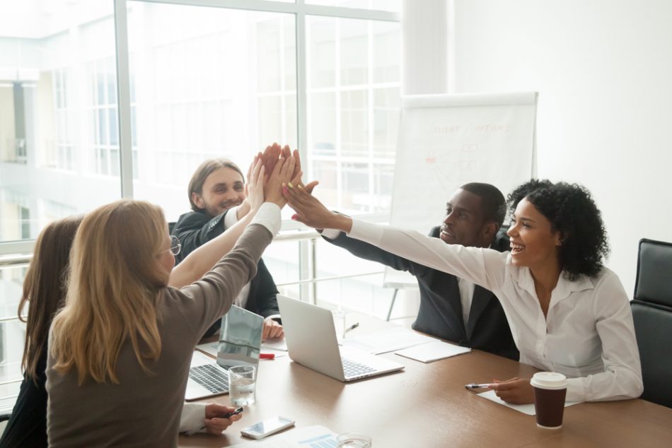 Excited african and caucasian business team giving high five at office meeting motivated by victory, achievement or good work result, multi-ethnic employees group celebrate corporate success together.