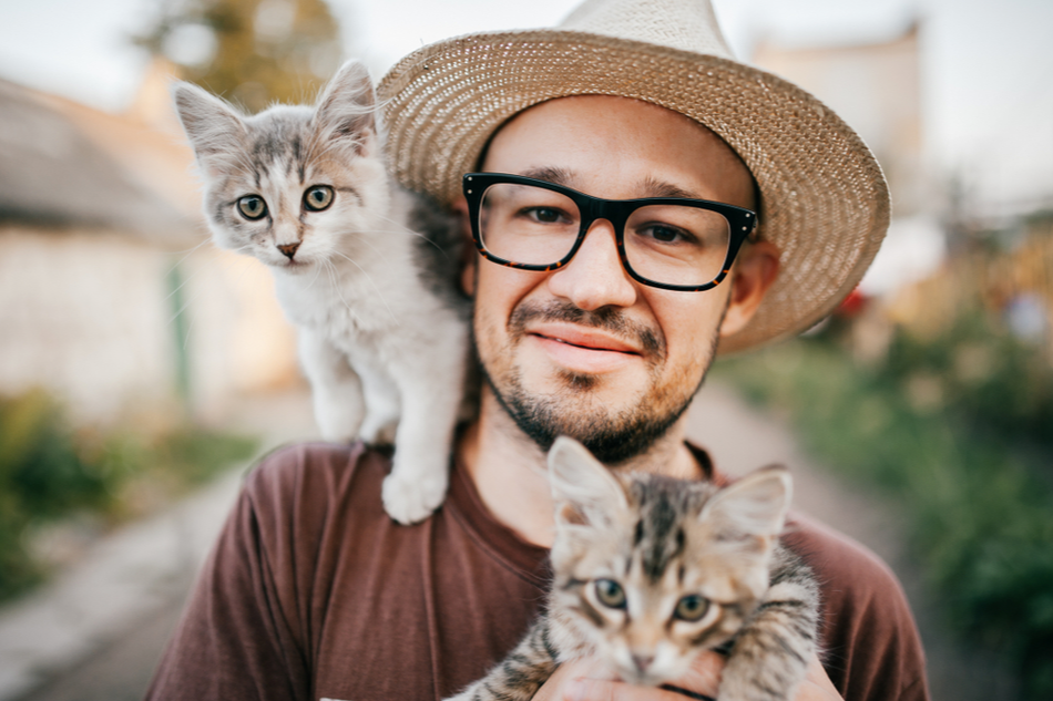 happy young man with hat and glasses carries two cats