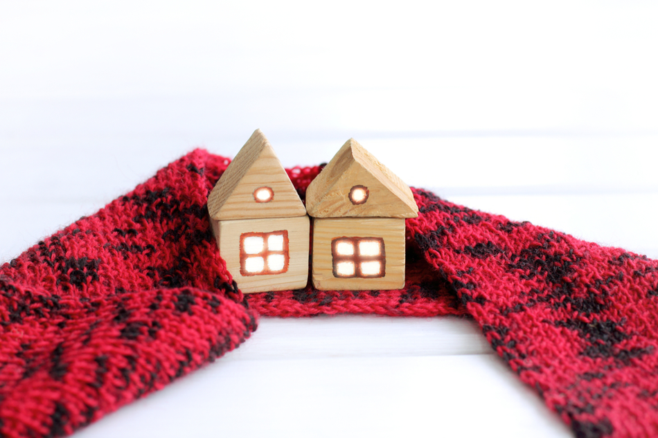 two tiny wooden house models wrapped in warm red material against white backdrop