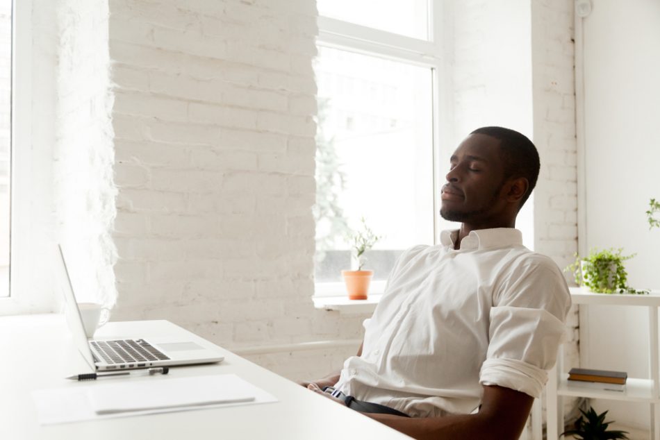 African american man relaxing after work breathing fresh air sitting at home office desk with laptop, black relaxed entrepreneur meditating with eyes closed for increasing productivity at workplace.