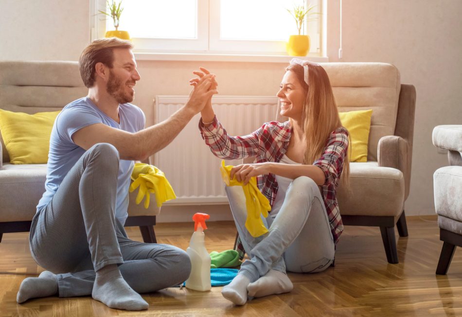 Couple is giving high five and smiling while sitting on the floor in living room after cleaning it.