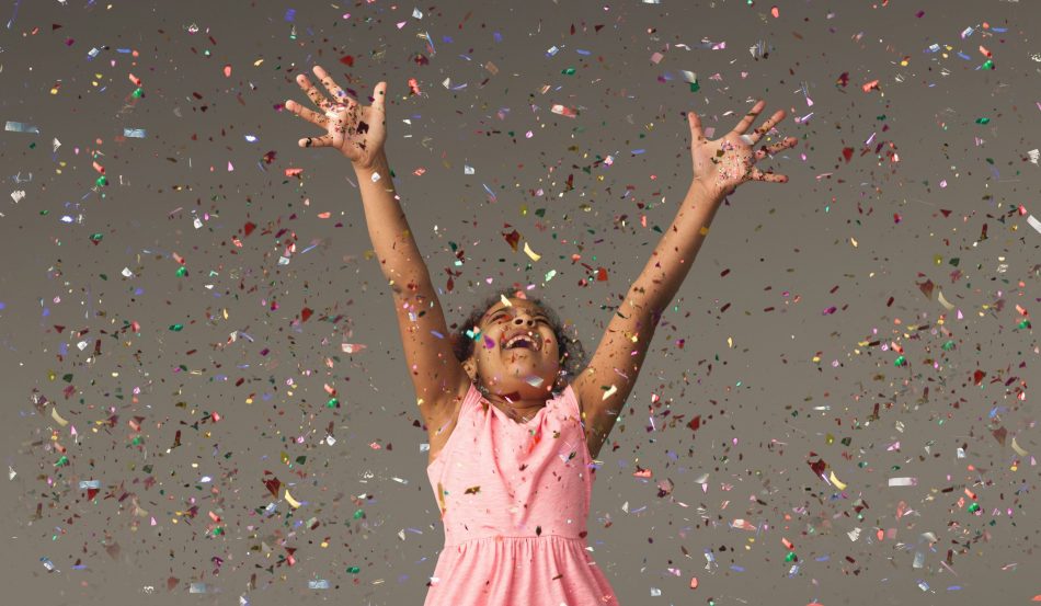 little girl in pink dress celebrates with confetti in the air