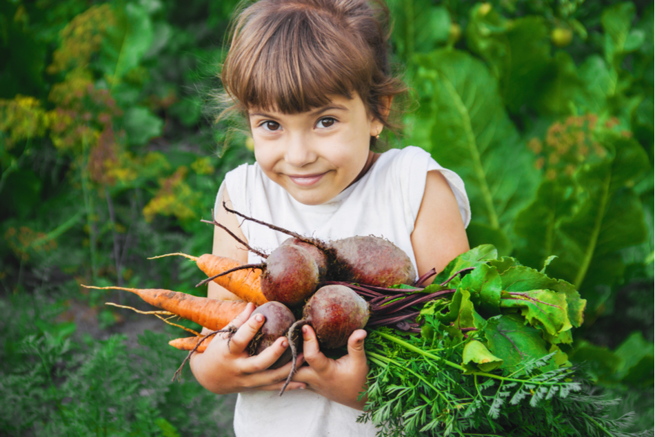 child happily holding home-grown vegetables
