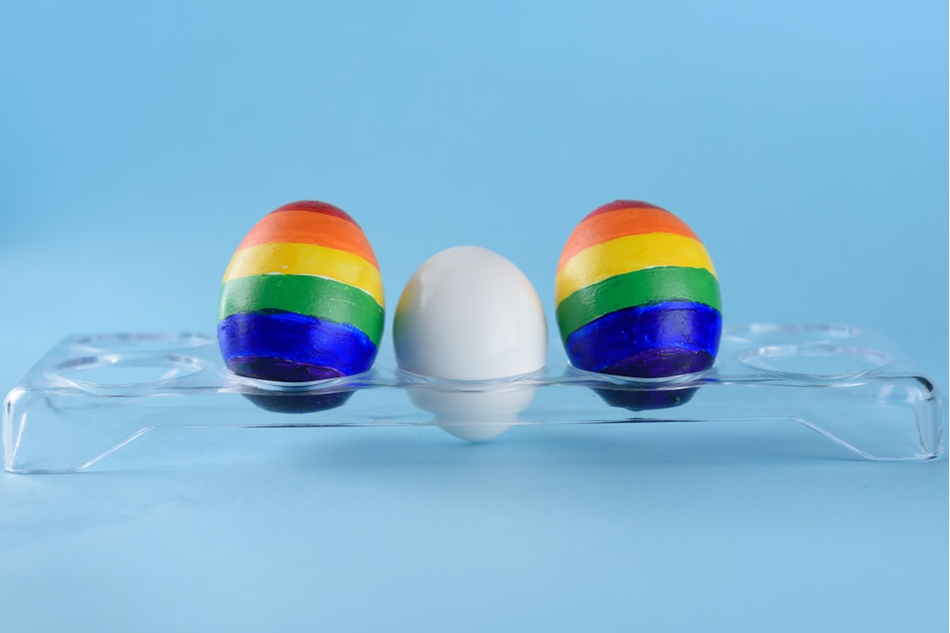 one white egg sits between two eggs painted in the LGBTQ rainbow