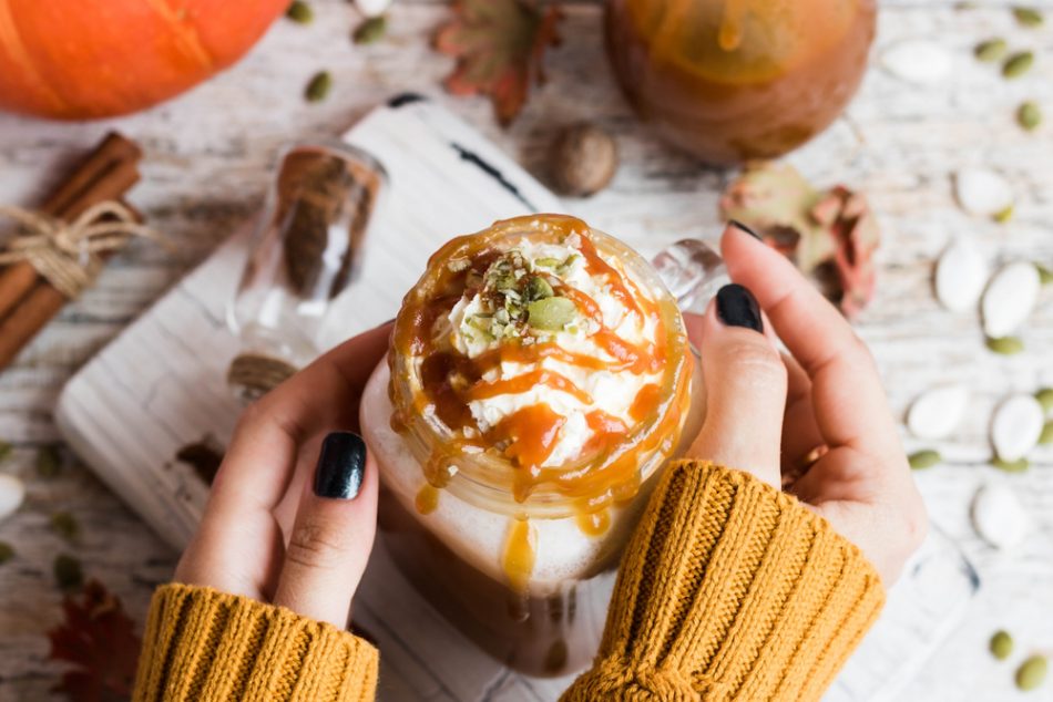 Female hands holding a pumpkin spice latte on a festive table