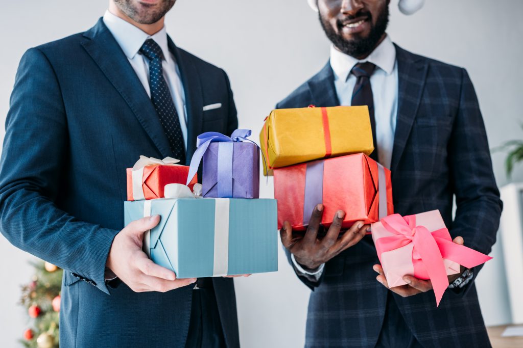 two men in business attire with their hands full of wrapped gifts