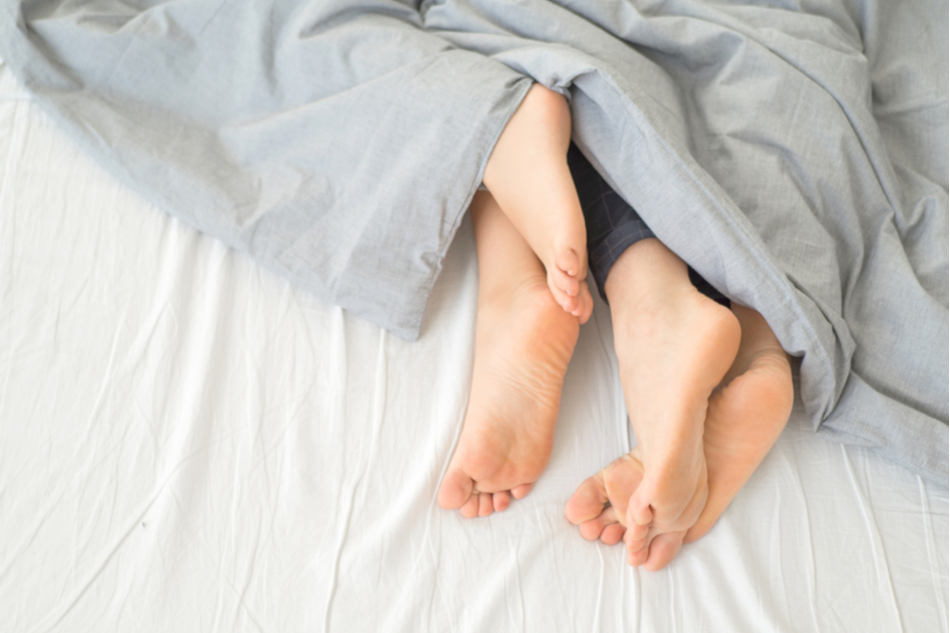 two pairs of feet in bed under covers