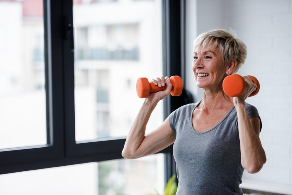 mature woman with two orange weights in her hands, strength workout at home