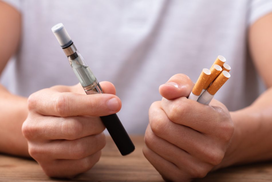 Person holding cigarettes in one hand and an e-cigarette in another.