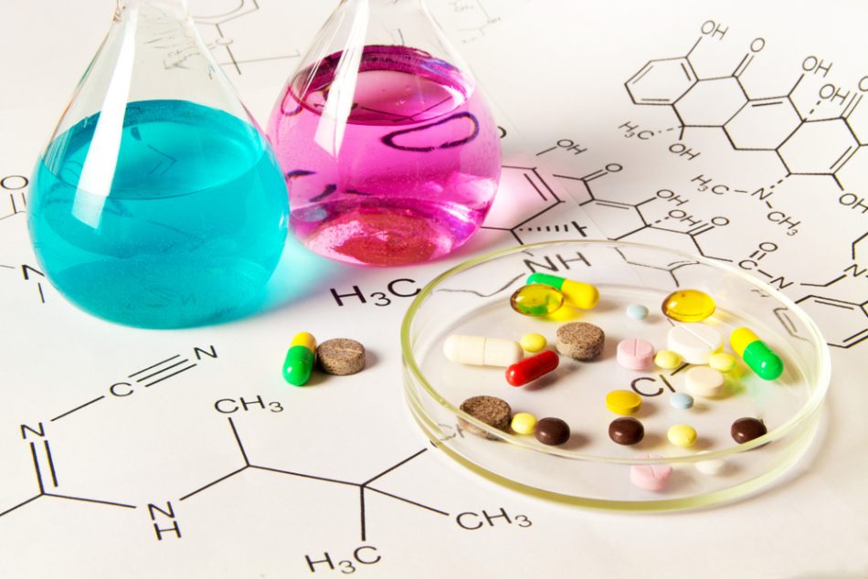 Representation of drug discovery process in laboratories, pink and blue liquid on top of chemical structures next to petri dish of multi-colored pills.