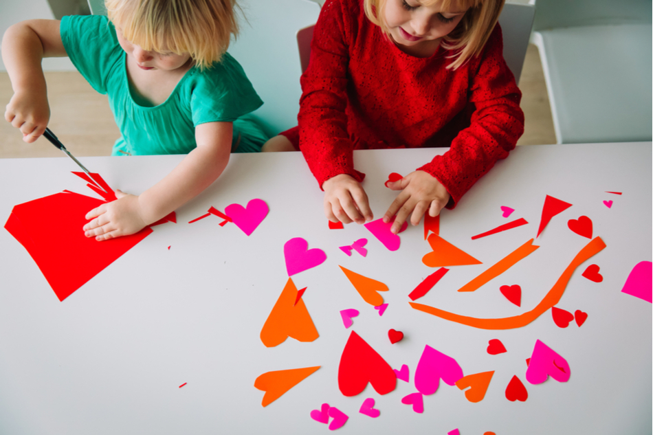 Two children cutting out paper hearts for valentines day craft