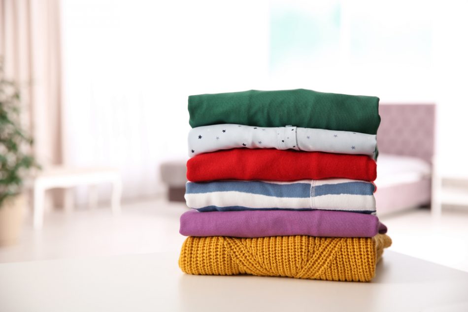 Stack of folded bright clothes on table against blurred background.