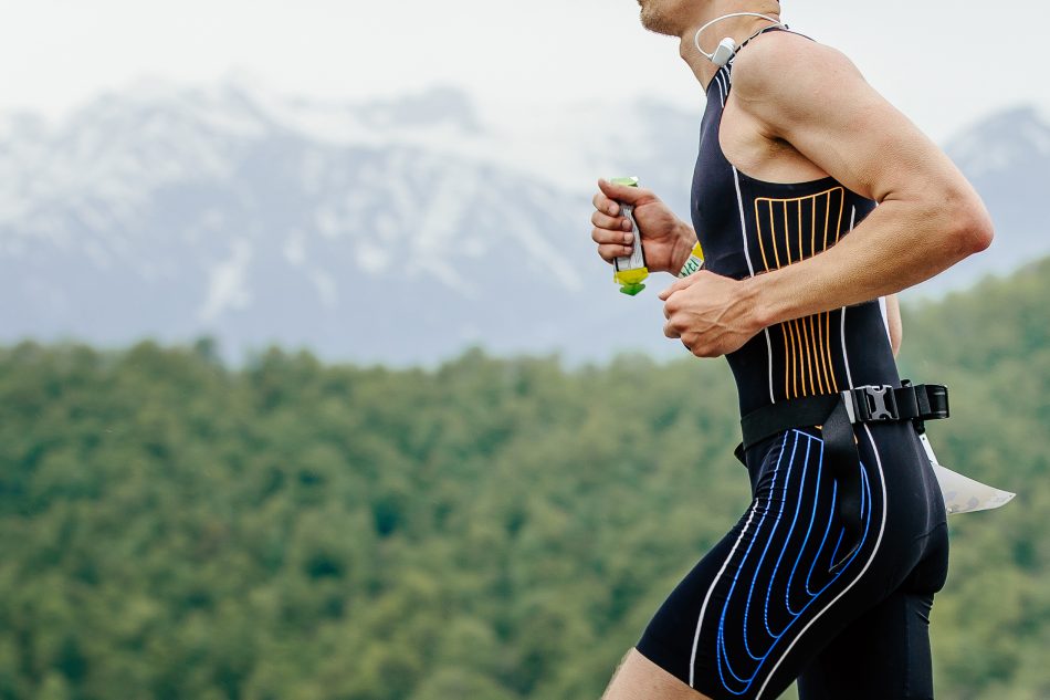 male athlete runner with energy gel in hand running on mountain marathon