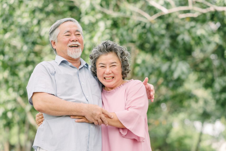 Happy Asian senior couple laughing and smiling while holding each other outdoor in the park.