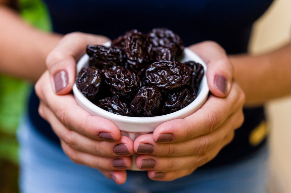 woman's manicured hands hold bowl full of prunes