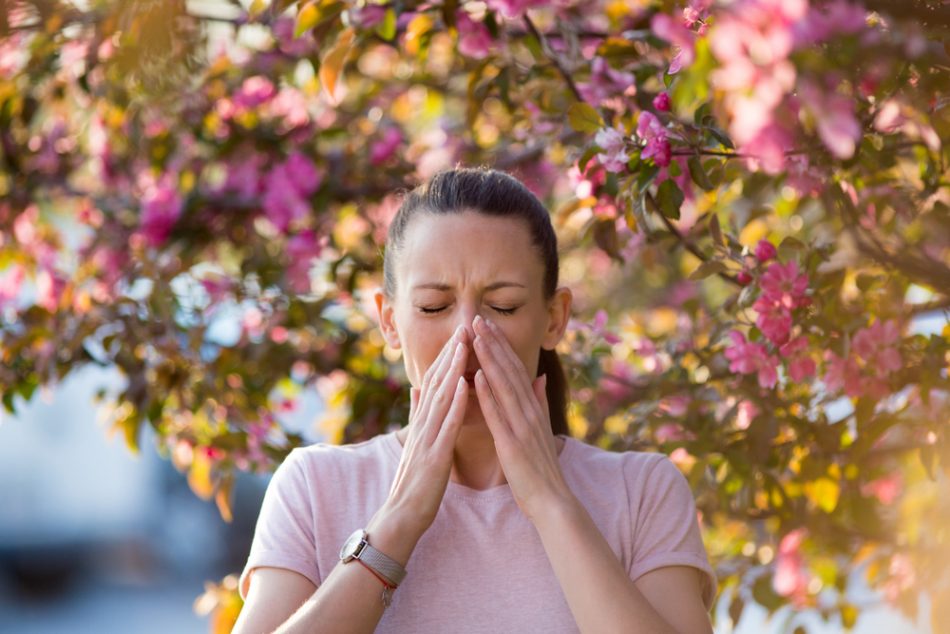 young woman sneezes in hands outside under tree with blossoms