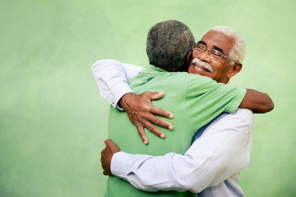 Two men hugging in front of a green background signifying friendhsip.