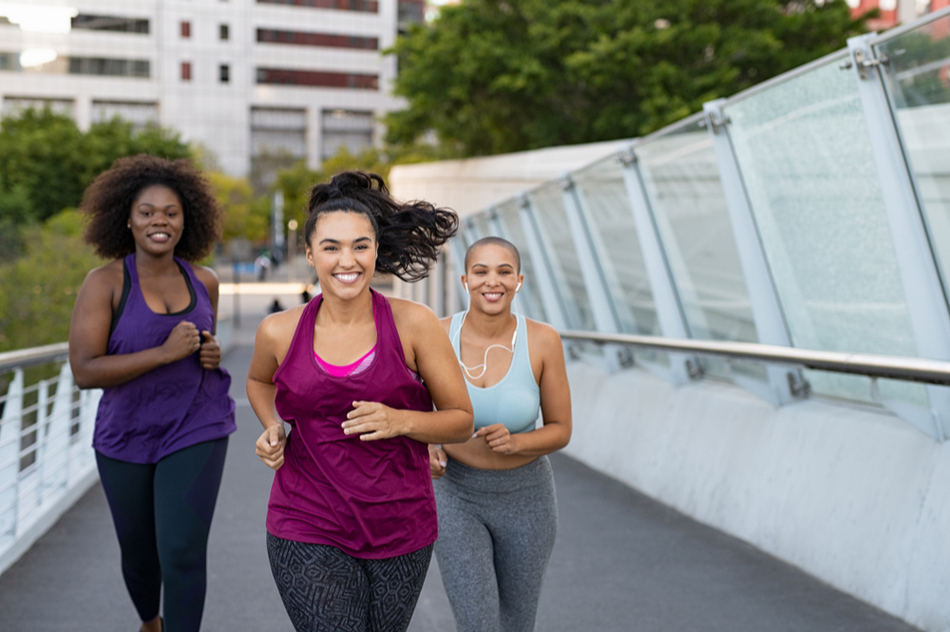 Three women smiling while running on a bridge