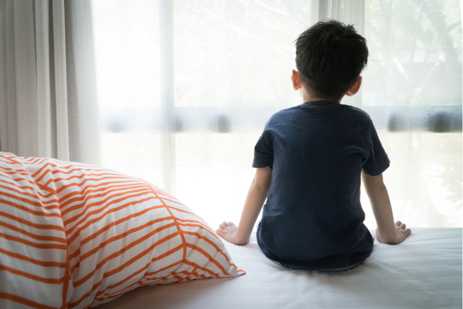 Little boy sits on bed alone on bed