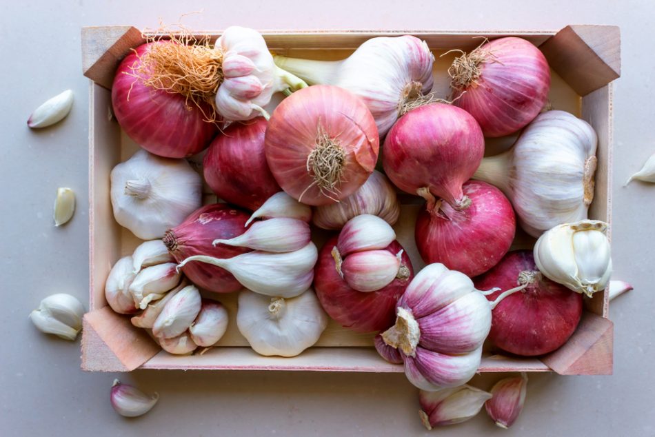 Young garlic and red onions in a vegetable box.