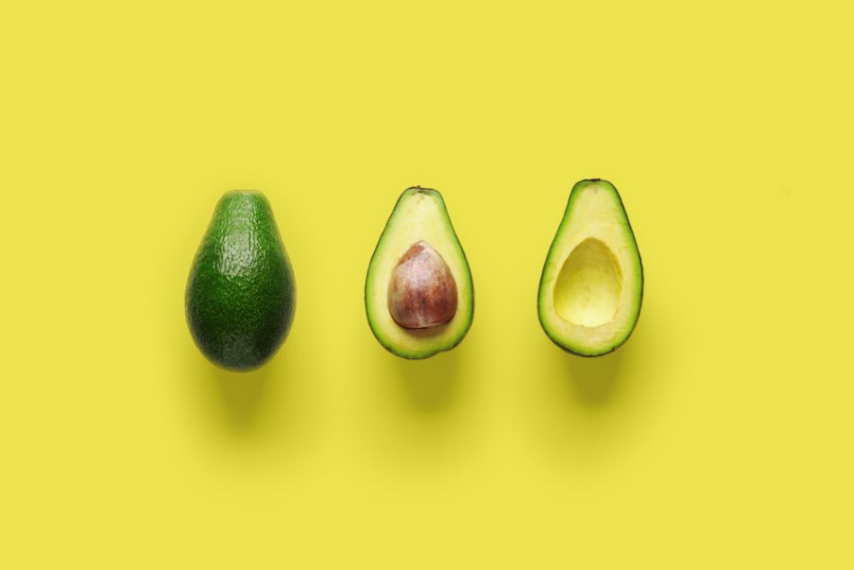 Whole avocado fruit and two halves in a row isolated on yellow background.