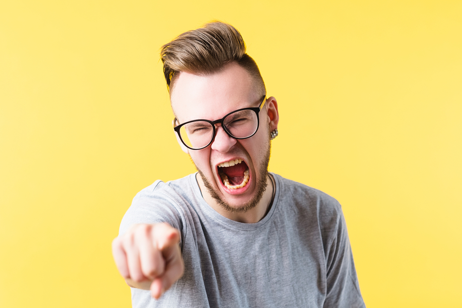 White man with glasses against a yellow background points finger and loses temper