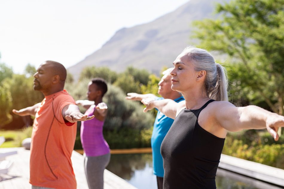 Group of senior people with closed eyes stretching arms outdoor in Pilates class