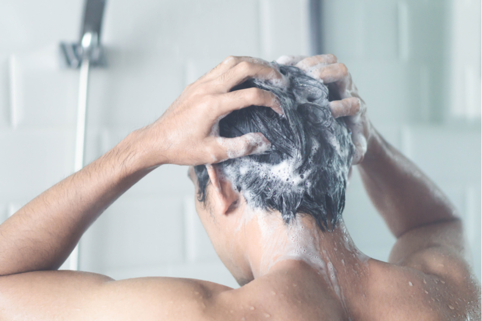 Man with dark hair lathers shampoo in the shower