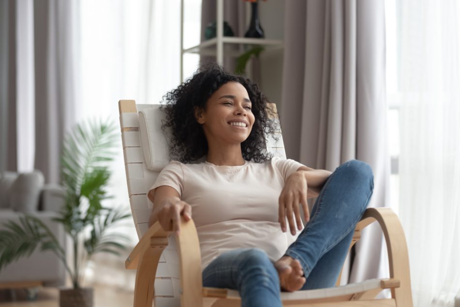 Smiling calm young woman relaxing on comfortable wooden rocking chair in living room.