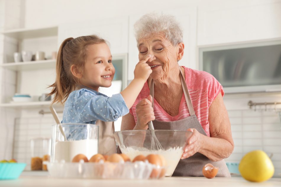 Cute girl and her grandmother cooking in kitchen.