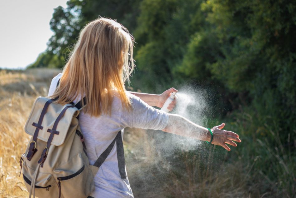 Woman with blonde hair applying mosquito repellent on hand during hike in nature.