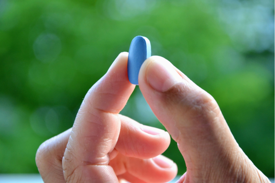 Man's hand holds Viagra pill against a blurred natural green backdrop