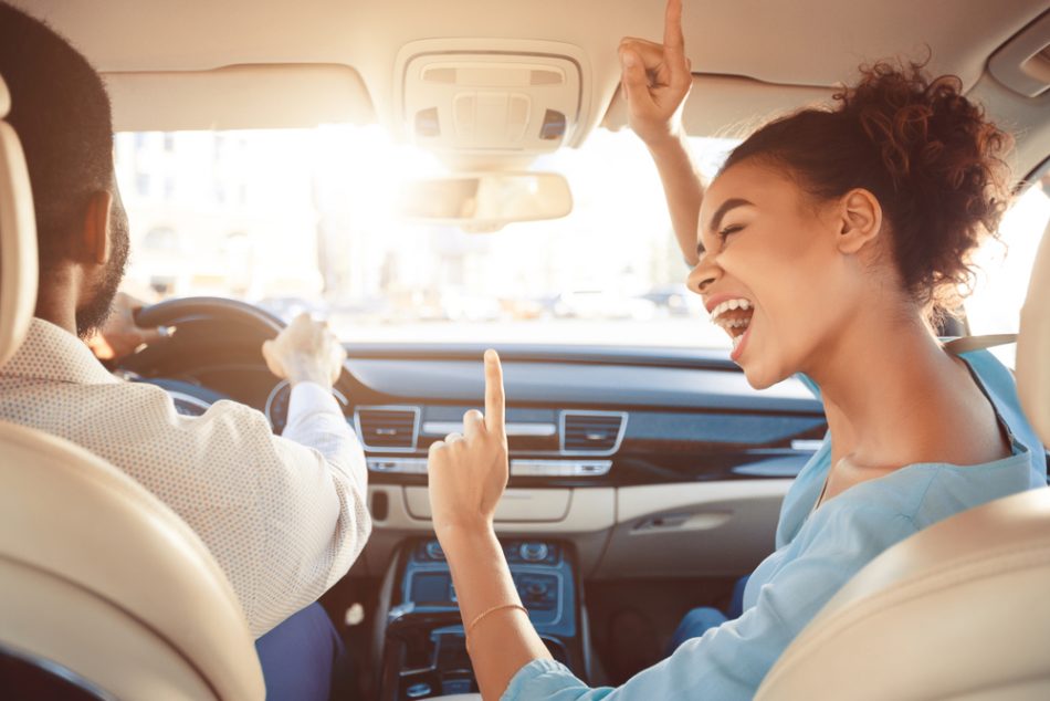 Happy couple, woman wearing blue shirt, driving in car and girl singing song, enjoy tavel by auto