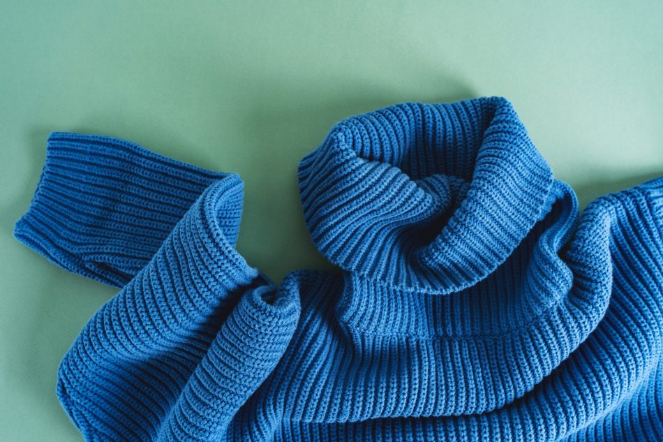blue knit sweater lays on top of mint green background