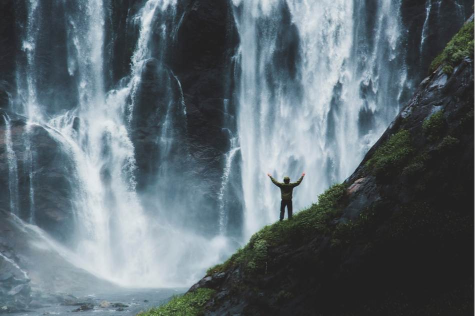 Hiker facing waterfalls rising his hands in amazement