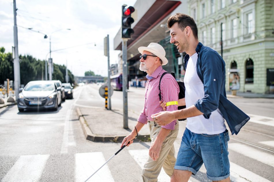 young man helps elderly blind man cross the road