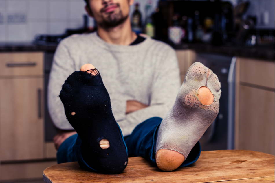 man sits with feet on the table, showing off holes in his socks