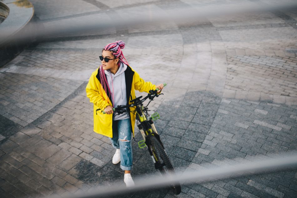 Woman in yellow coat walks her bike on the street