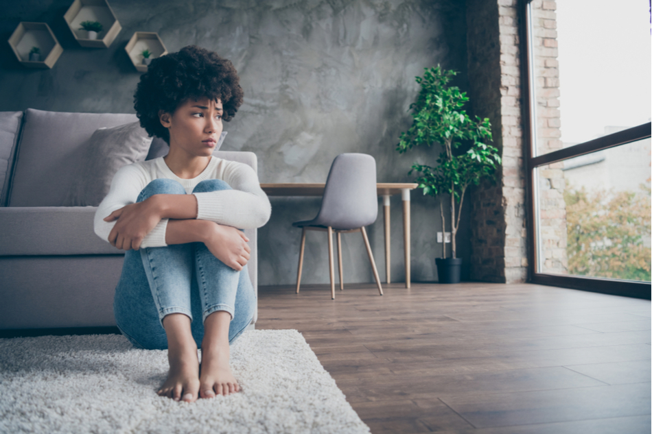 Young woman with afro sits on the floor of her living room
