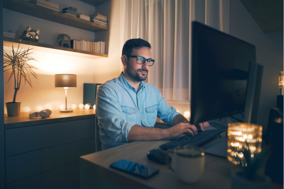 Young man with glasses sits in front of computer and sends work email