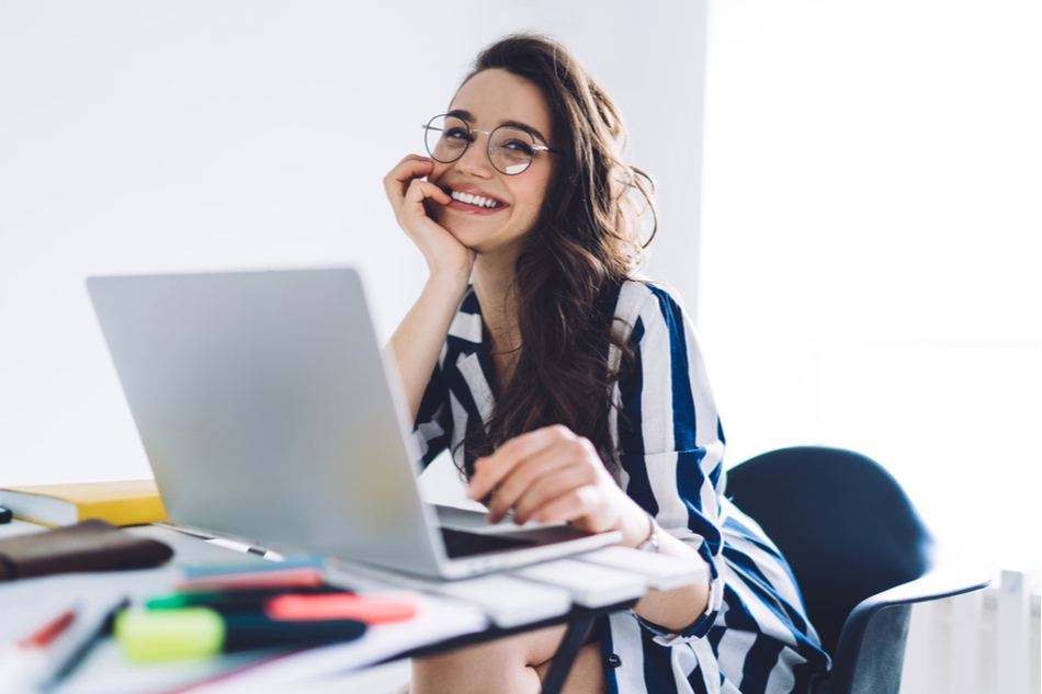 Attractive young woman professional with glasses smiles while working on laptop