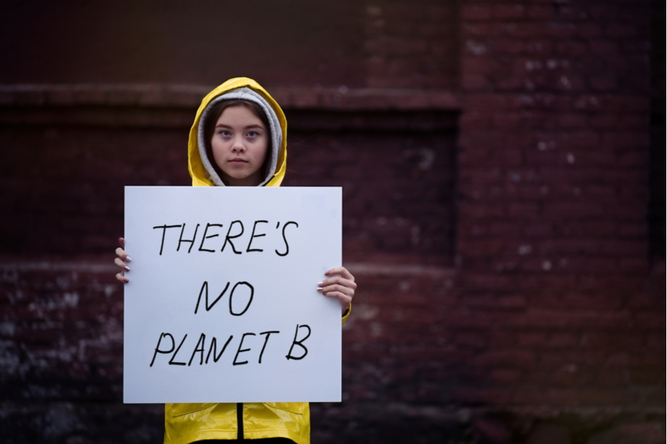 child in yellow rain coat holds sign reading: THERE'S NO PLANET B