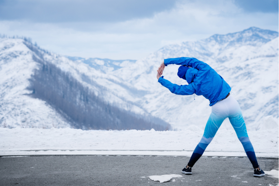 man stretches outside in the winter with mountains in the background