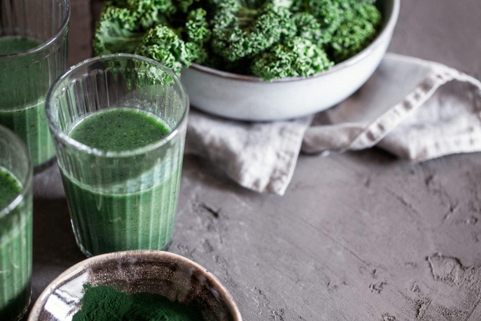 A healthy vegan drink green kale smoothie with spirulina for detox on dark background close-up.